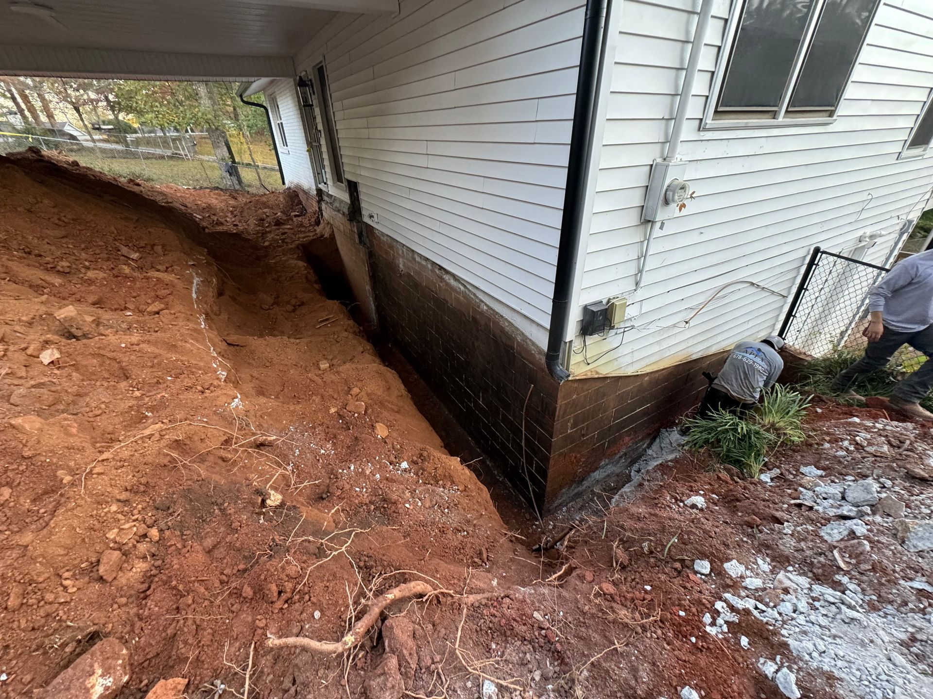 Construction site with a house, exposed foundation, and a person working.