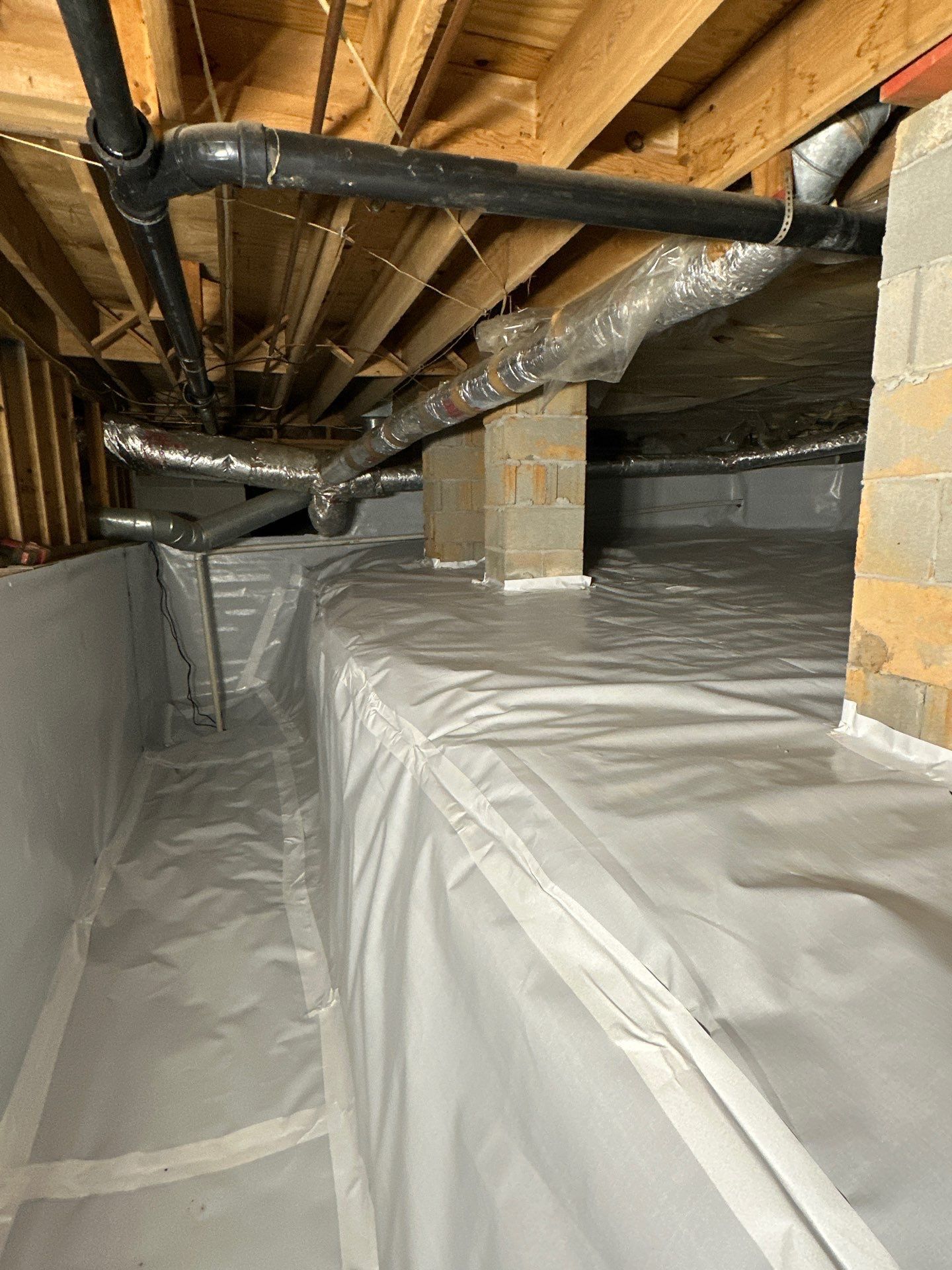 Crawl space with white vapor barrier covering the floor and walls, pipes, and ductwork visible above.