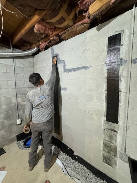 A man in a gray shirt is kneeling down in a basement.