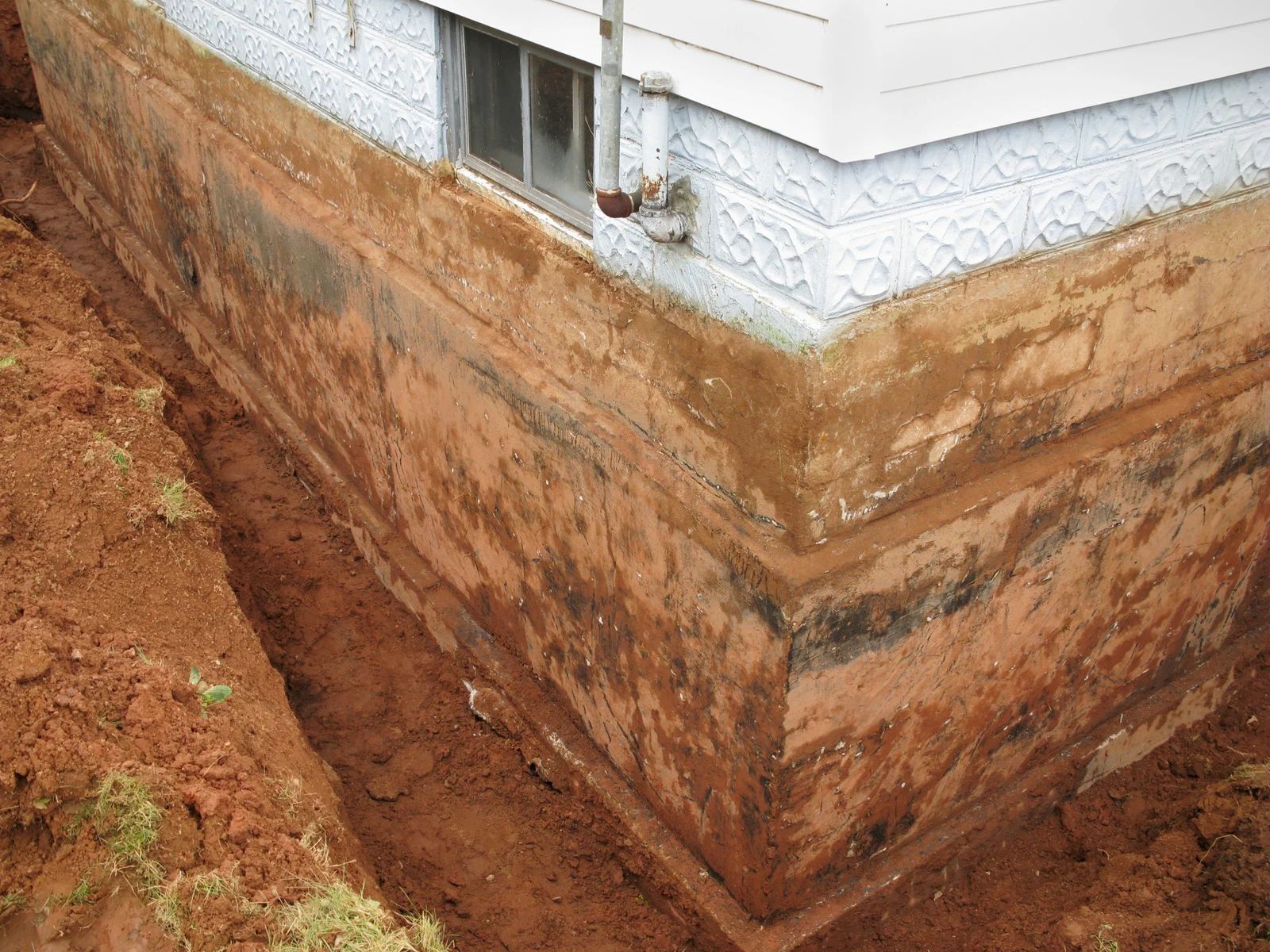 Exposed foundation of a white house with water-damaged, eroded soil along the base