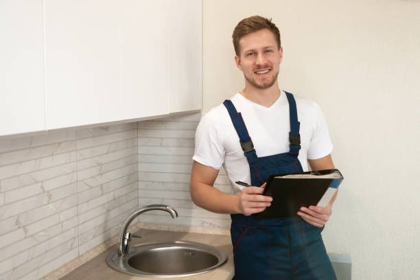 Plumber with clipboard inspecting kitchen sink and cabinets – home plumbing maintenance service.