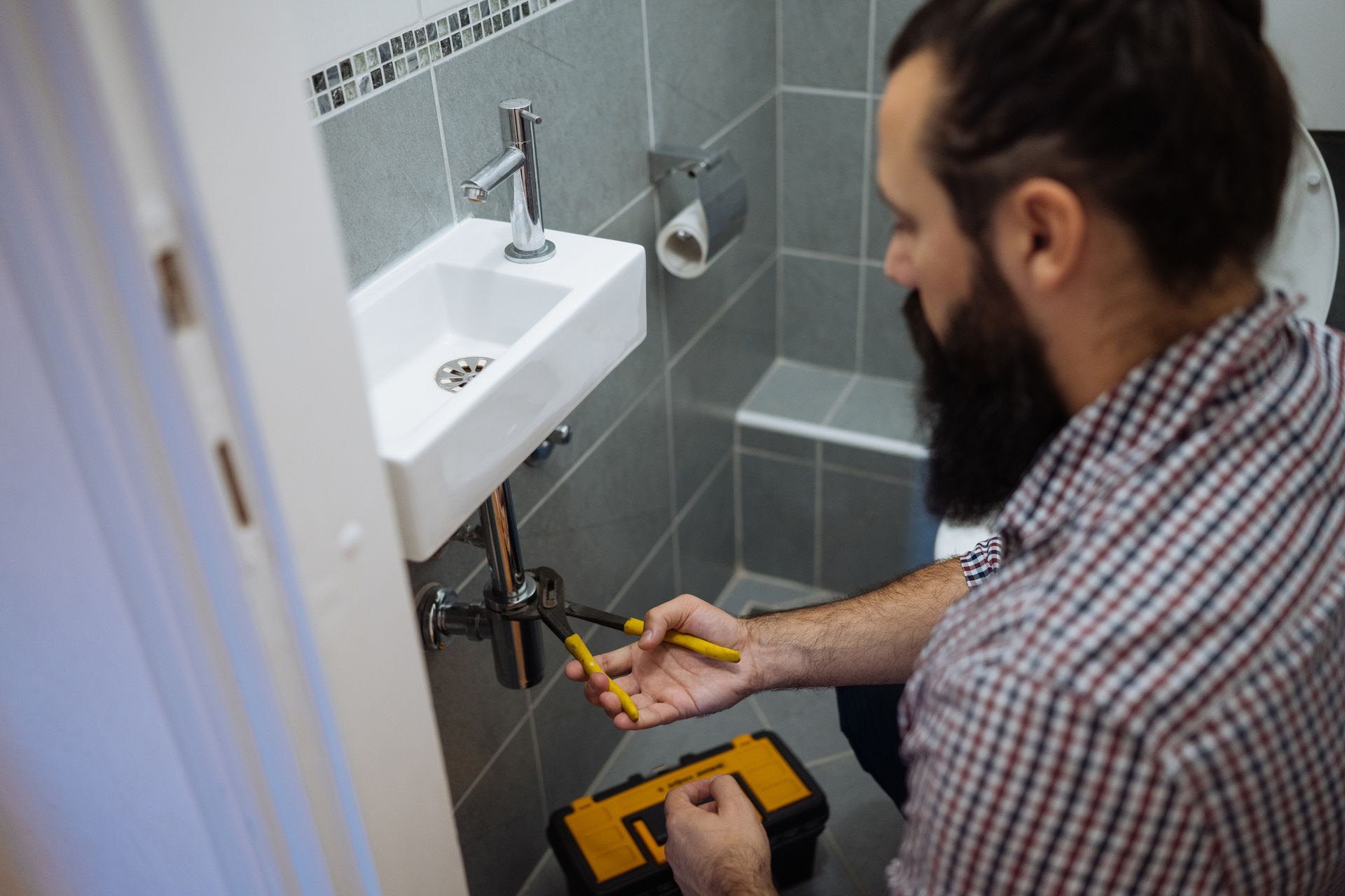 A plumber fixing under a bathroom sink at a customer’s home. A plumber fixing under a bathroom sink at a customer’s home.