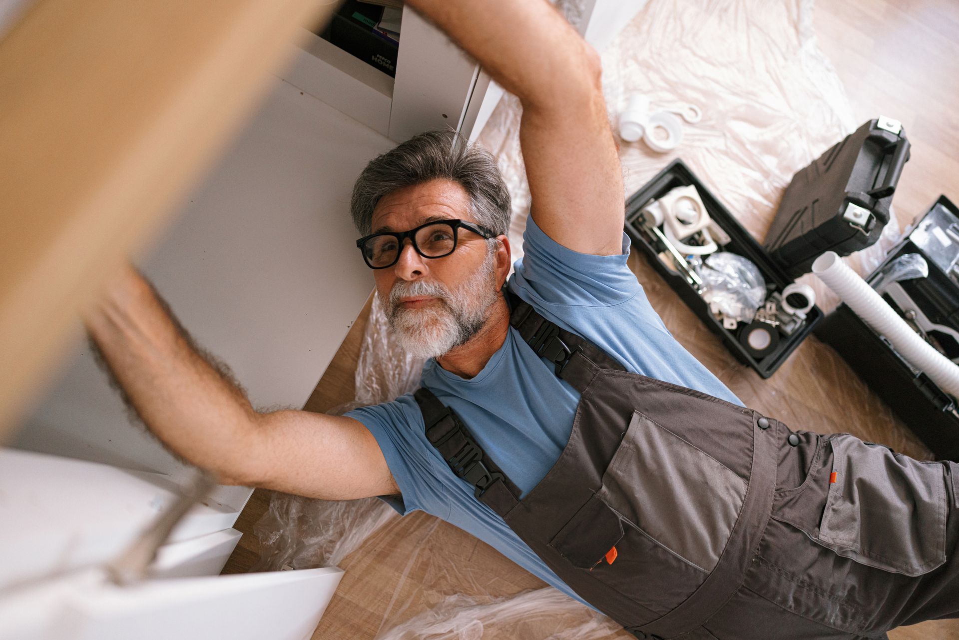 A plumber fixing a kitchen sink at a customer’s home. A plumber fixing a kitchen sink at a customer’s home.