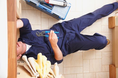Plumber lying on floor fixing sink with toolbox nearby. — Leaked Pipe in Tacoma, WA