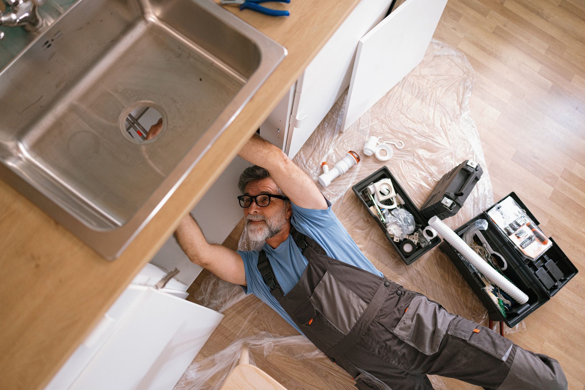 Top view of a plumber performing plumbing repair, fixing the sink in the kitchen.