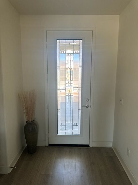 White entryway with a decorative glass door, vase with tall grass, and light wood flooring.