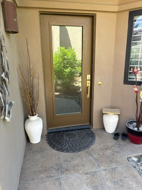 Tan entryway with brown door, plants, and black doormat.