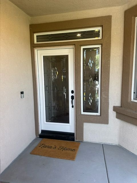 Exterior view of a home's entrance. White door with glass panels and side window. Welcome mat on the gray porch.