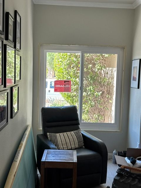 A dark recliner chair in front of a window, side table, framed art, and a light-colored wall.