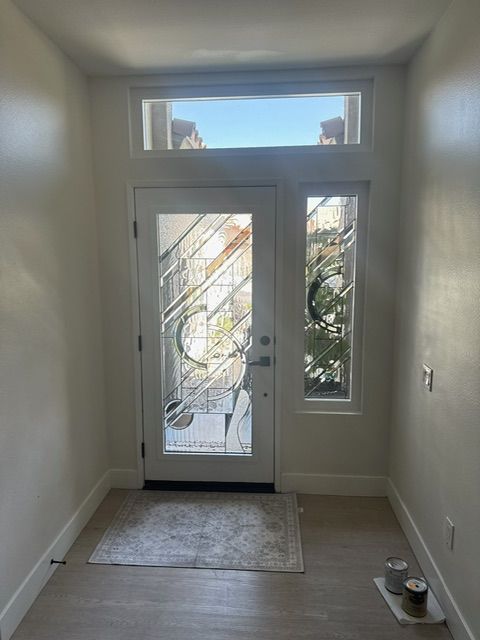 Entryway with white door, sidelight, and transom. Stained glass design, beige walls, and light wood floor.