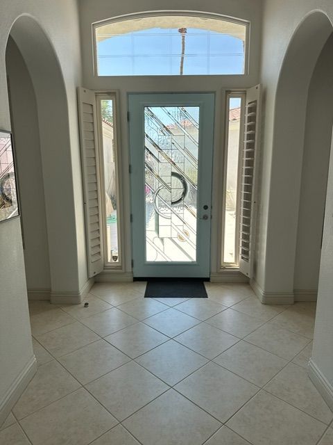 Entryway with arched doorway, light blue front door, side panels, and tiled floor.