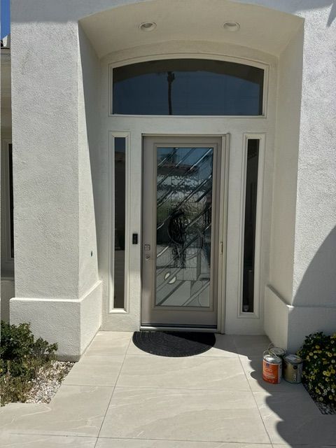 Front door of a home with a glass design, surrounded by white pillars and side windows; black doormat on the concrete path.