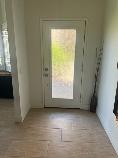 Entryway with frosted glass door, light wood-look tile, and tall decorative branches.