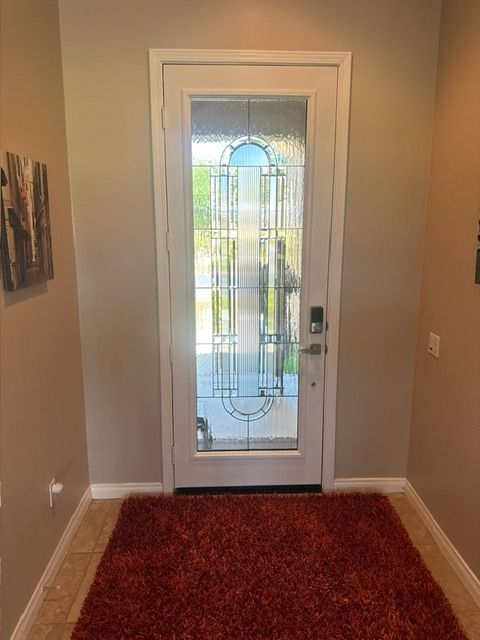 Entryway with red rug, white door with glass panels, beige walls, and brown tile flooring.