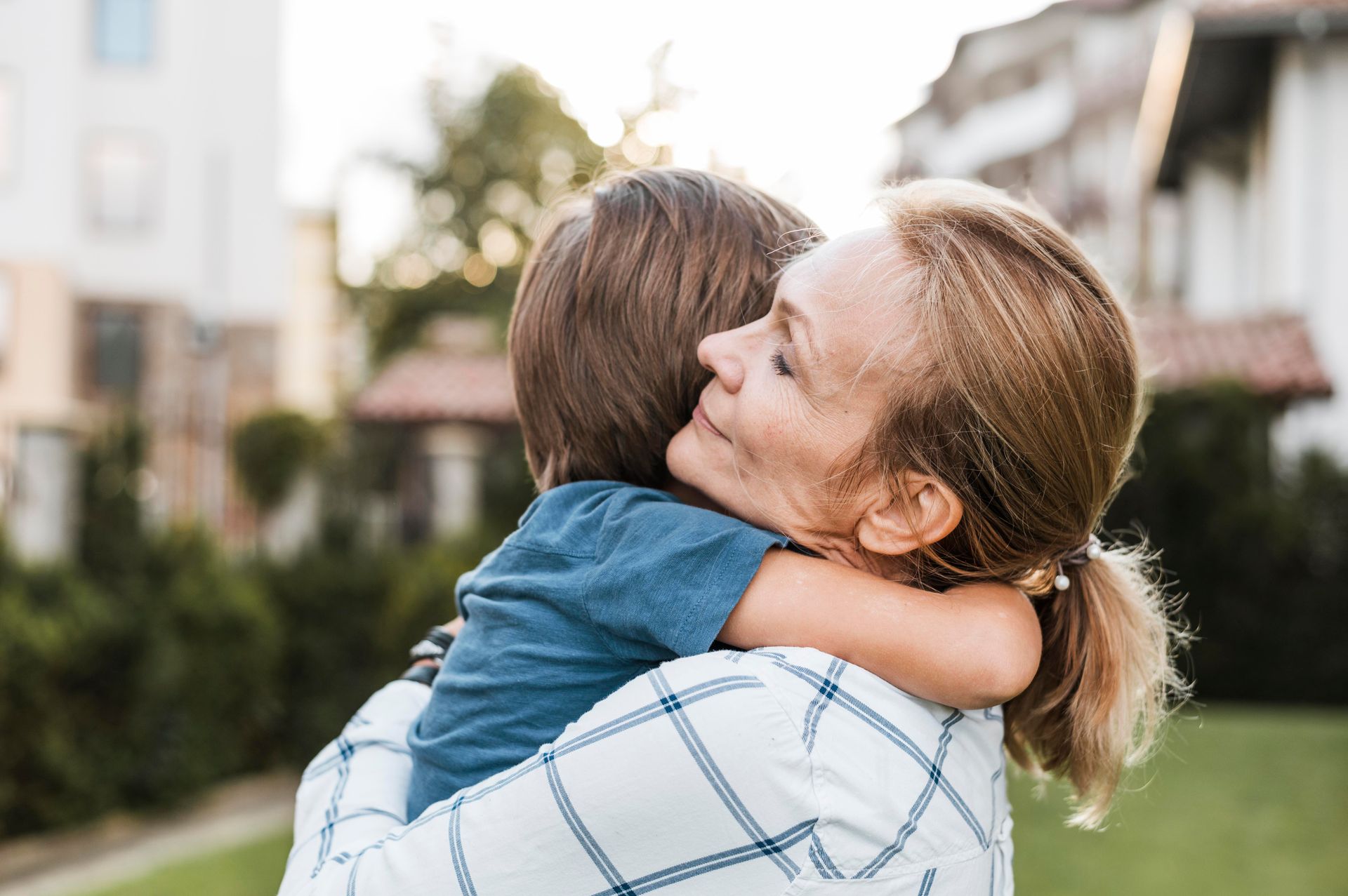 A woman is hugging a little boy in a park.