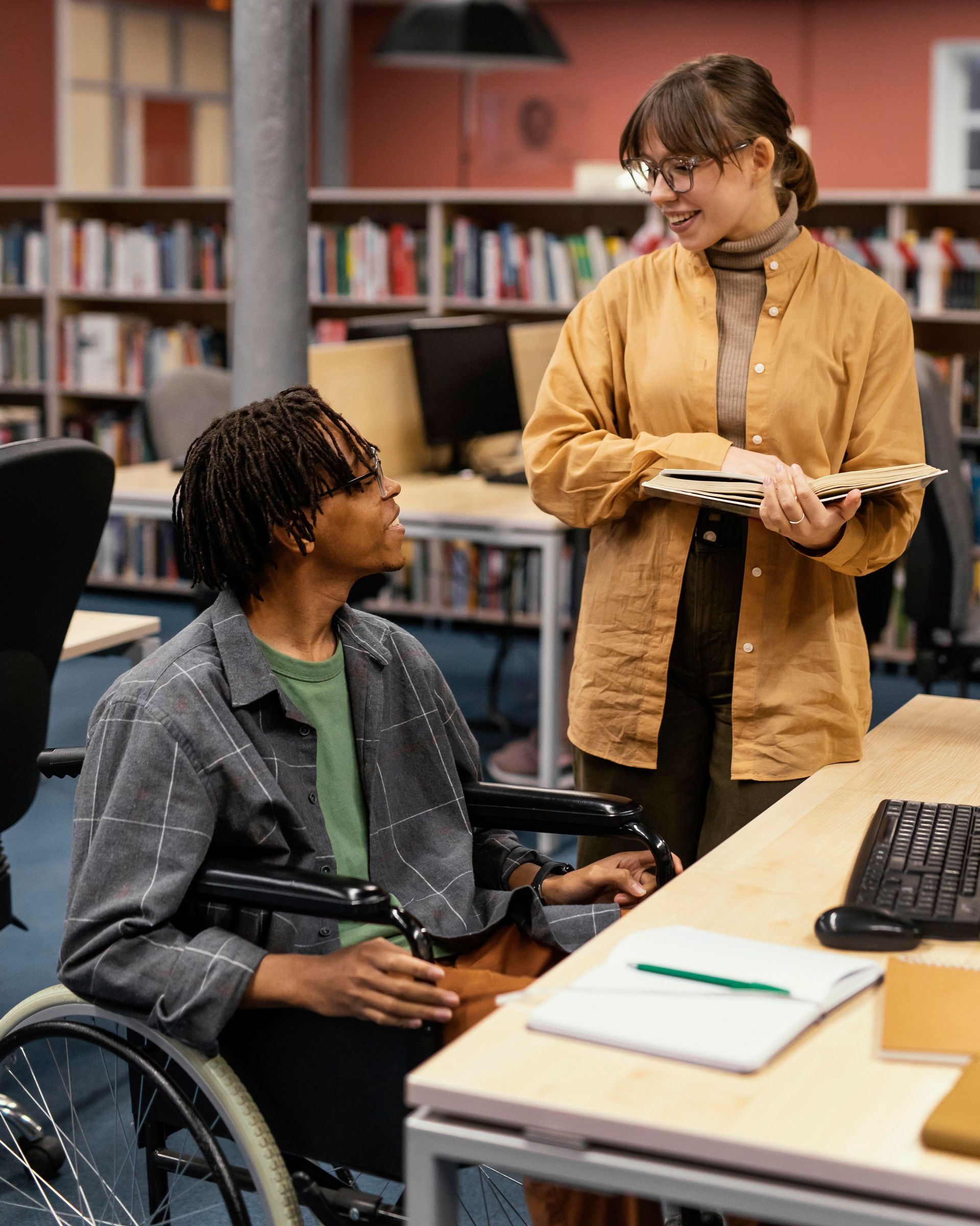 A woman in a wheelchair is talking to another woman in a library.