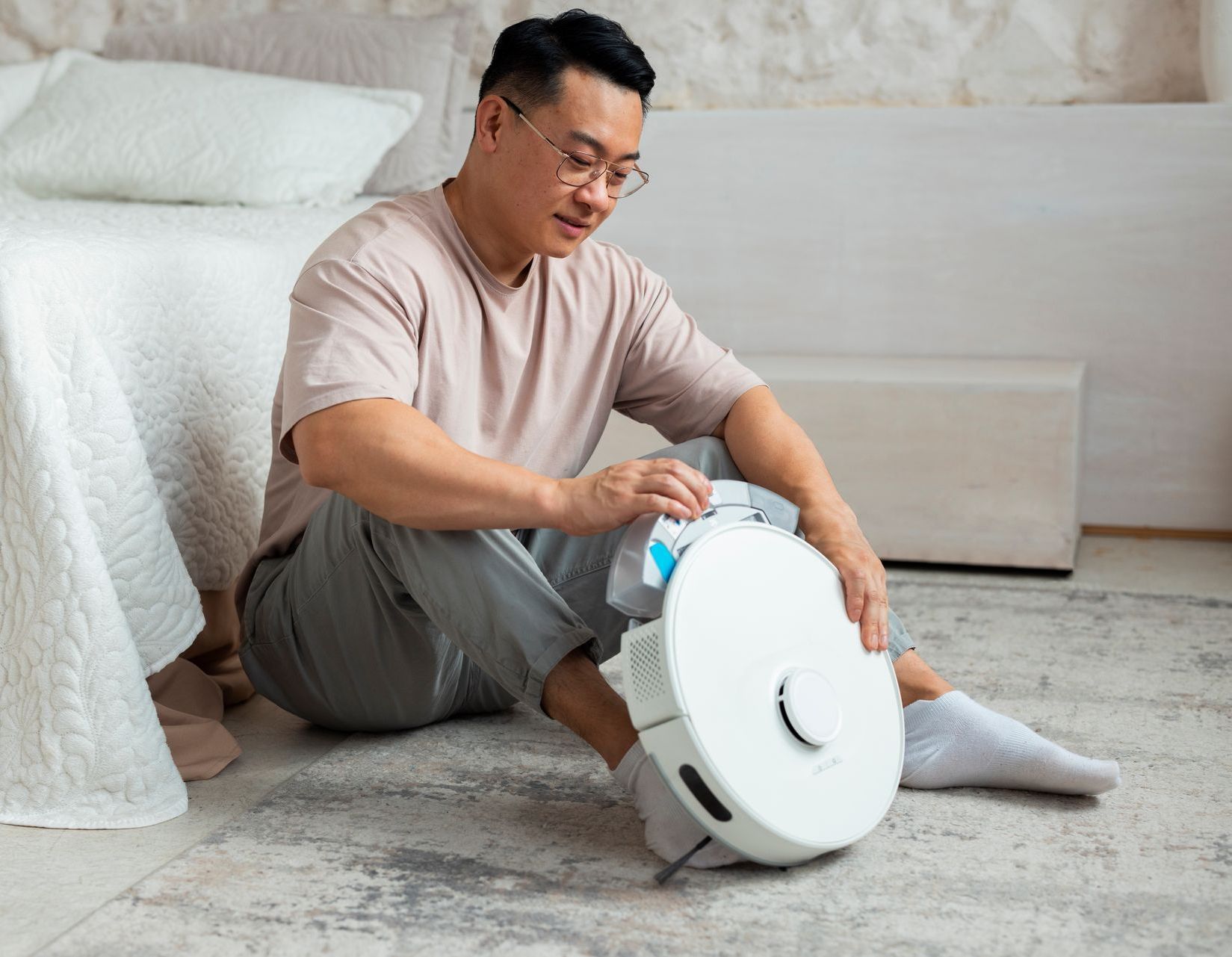 A man is sitting on the floor with a robot vacuum cleaner.