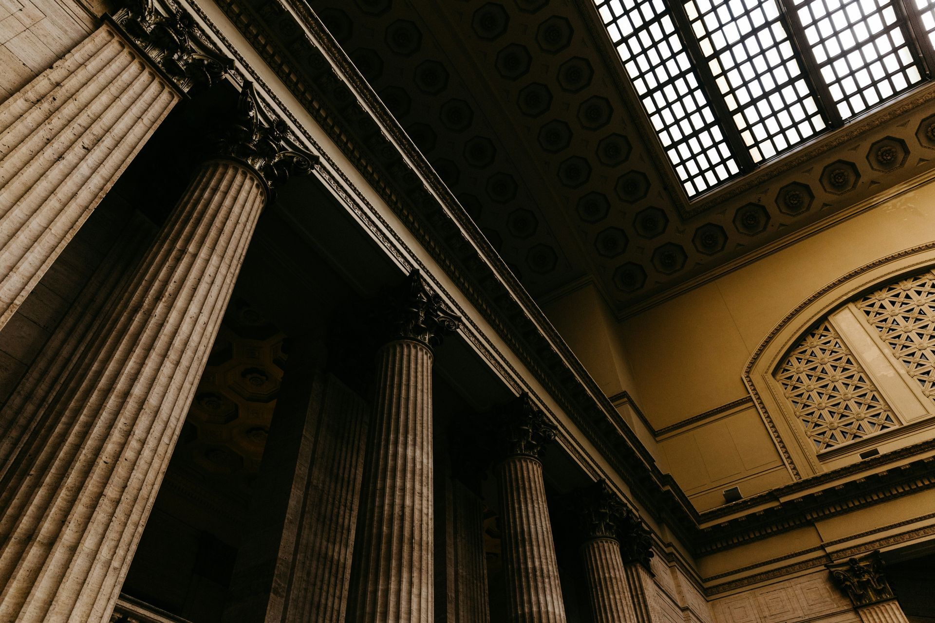 Looking up at the ceiling of a building with columns and a window.