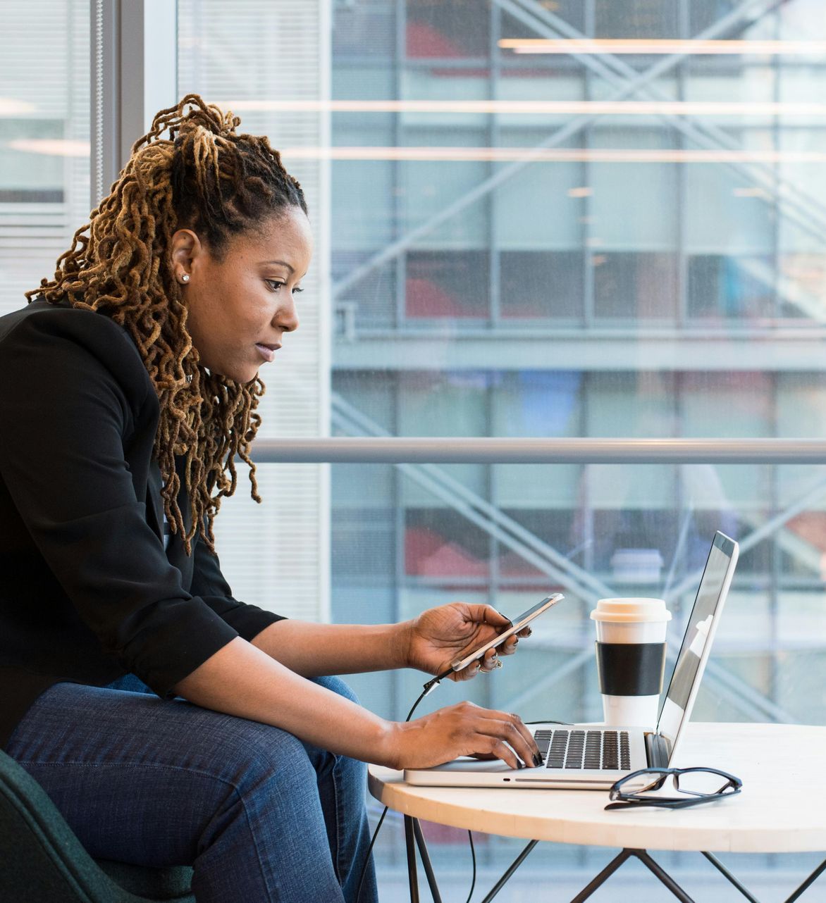 A woman is sitting at a table with a laptop and cell phone