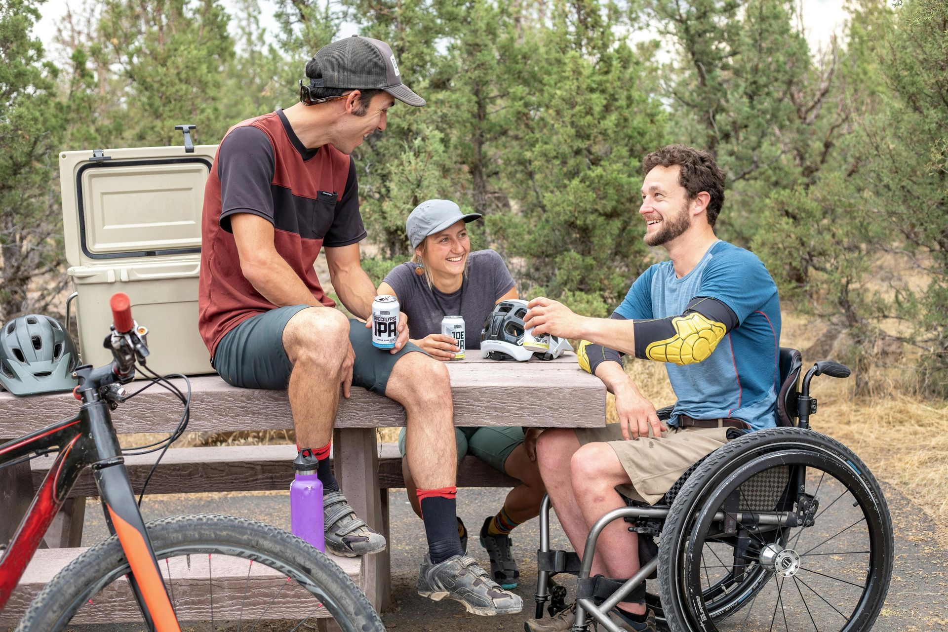 A man in a wheelchair is sitting at a picnic table with two other people.