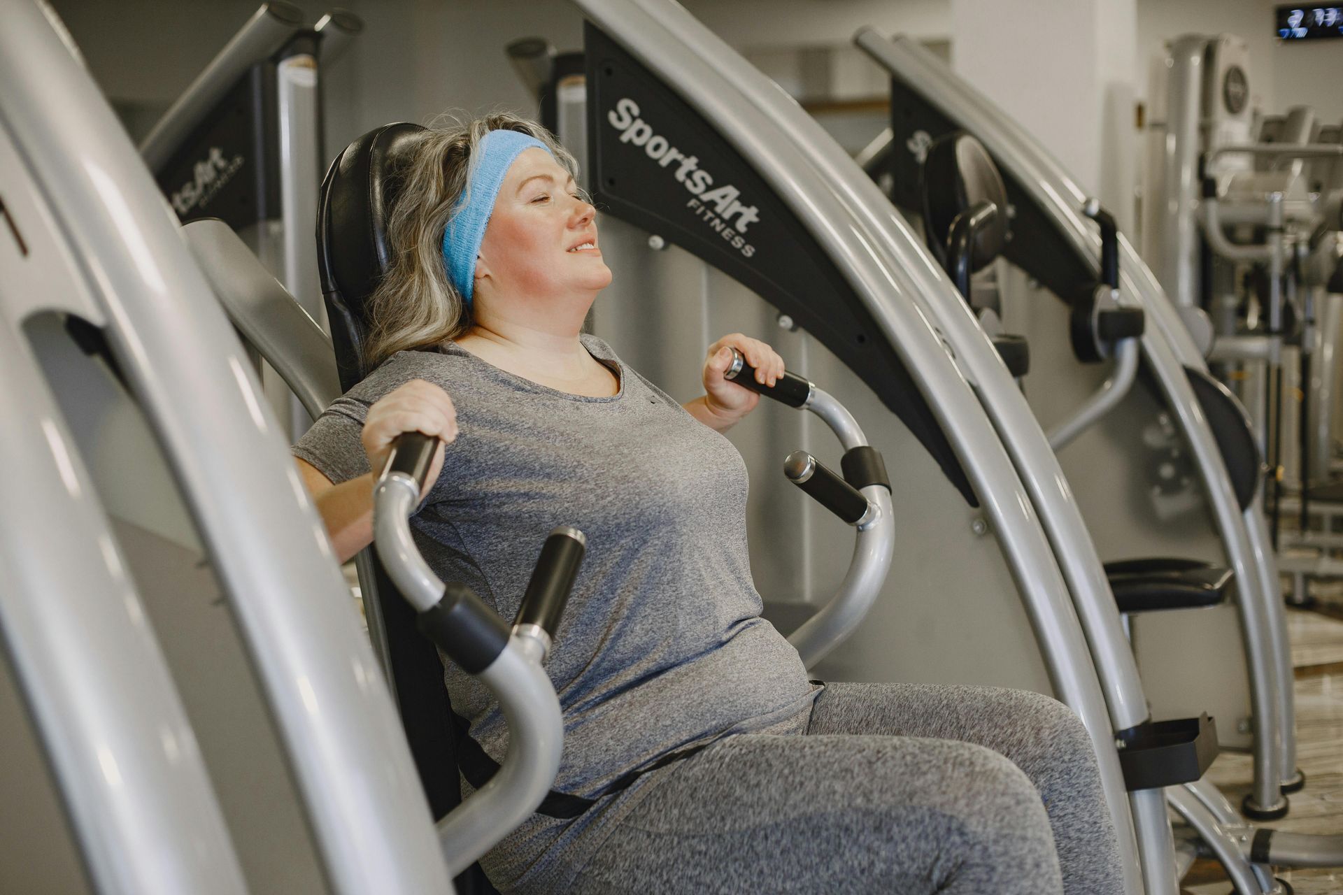 A woman is sitting on a machine in a gym.