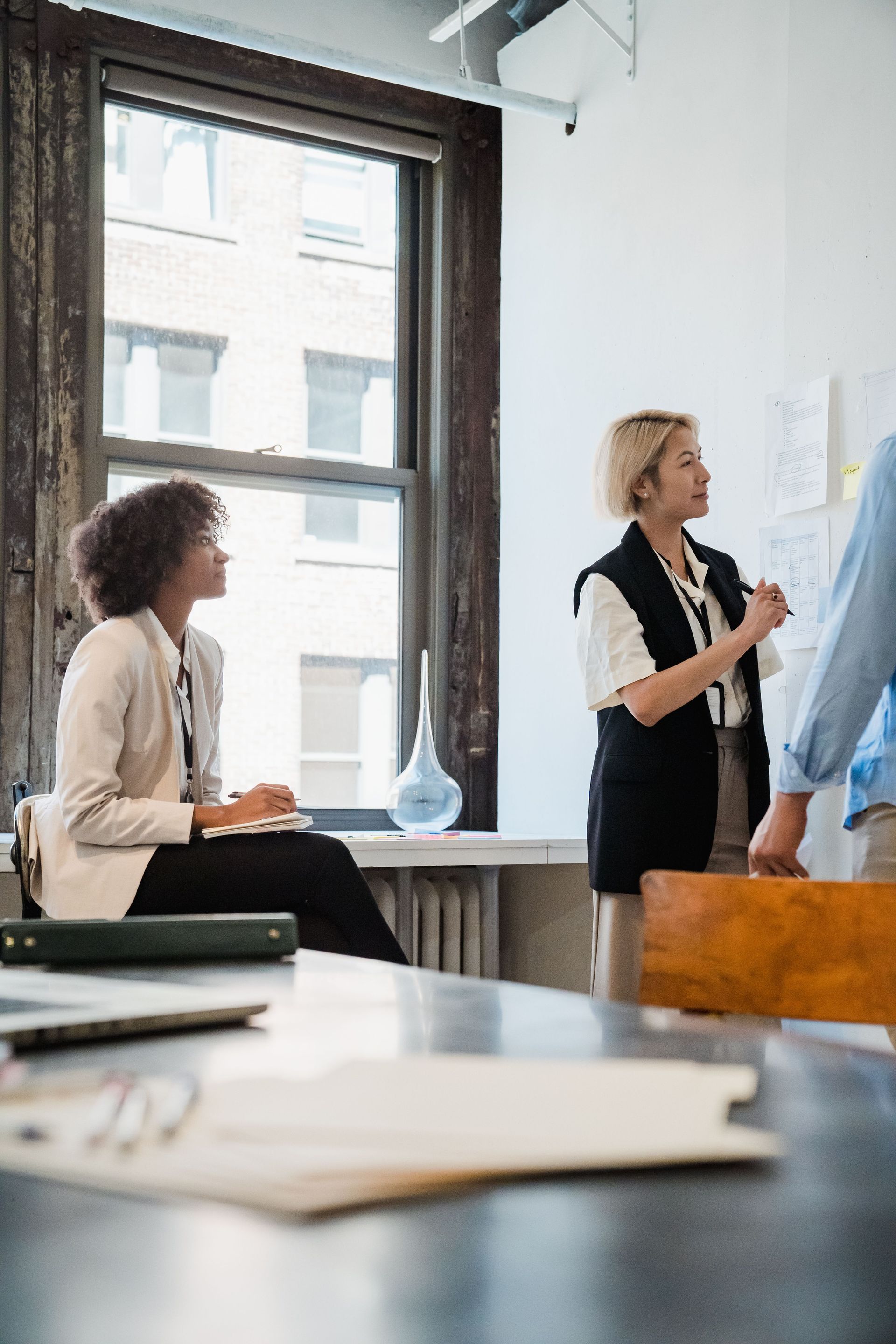Two people in a bright office discuss a large chart near a window