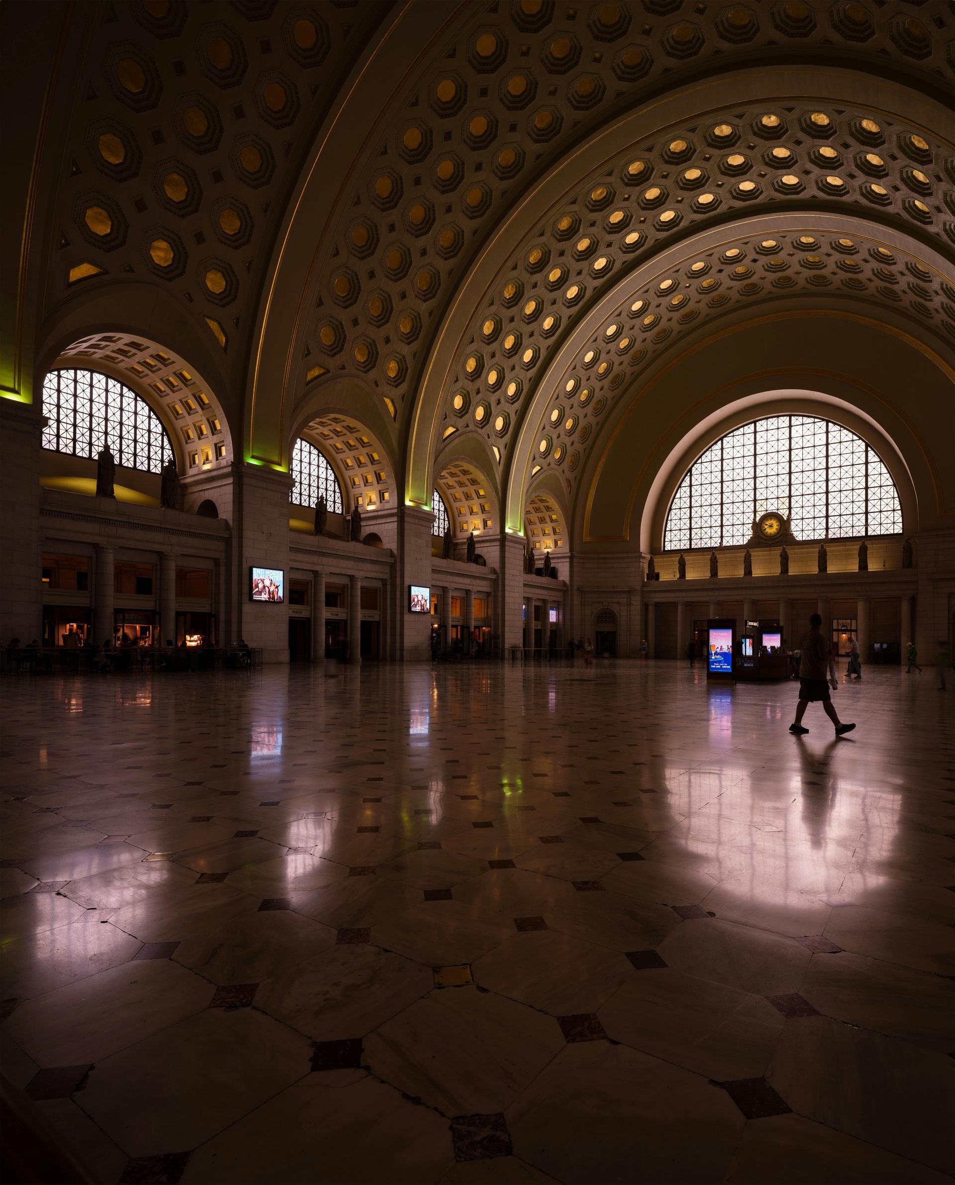 A person is walking through a large building with arched windows