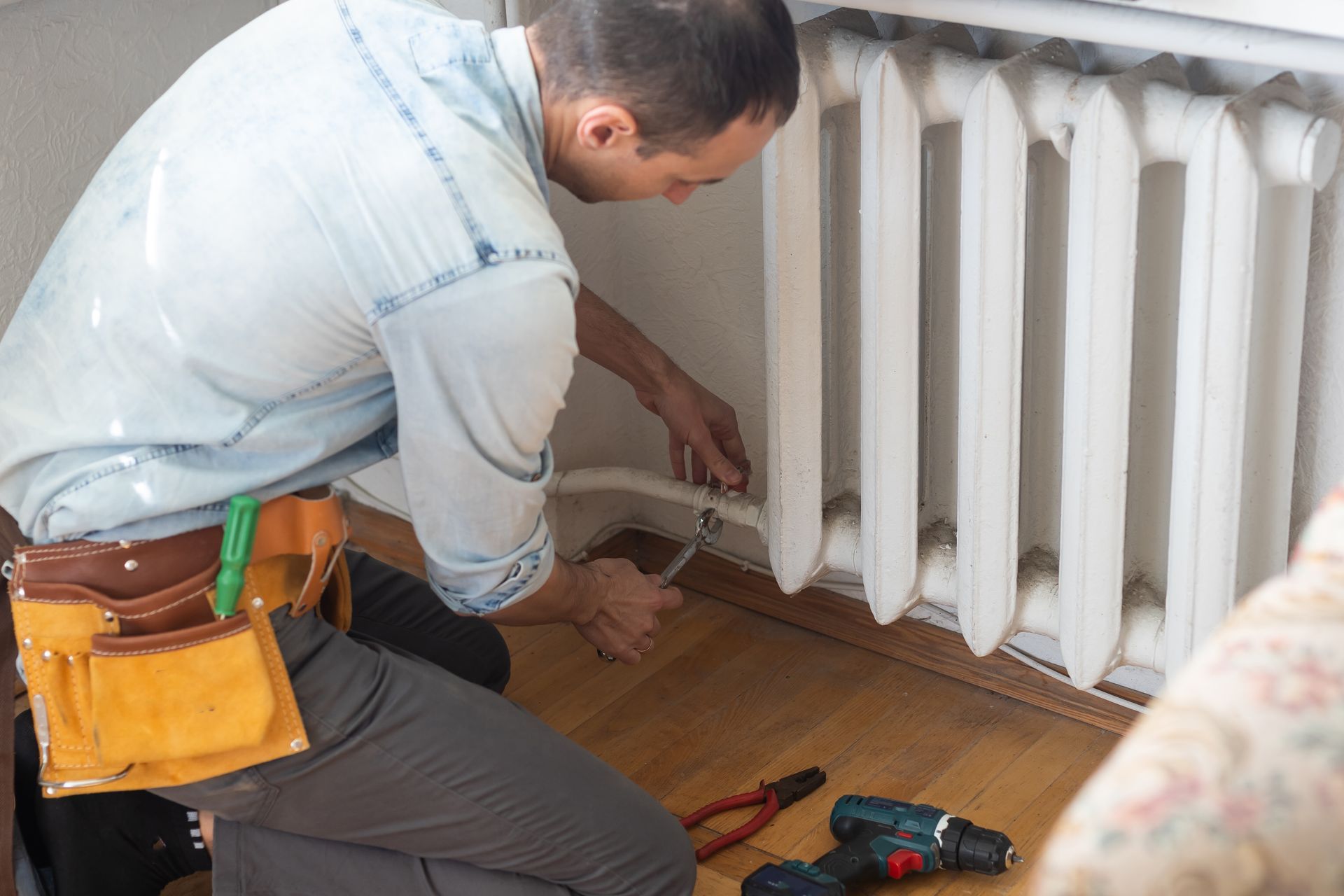 A man is kneeling on the floor fixing a radiator.