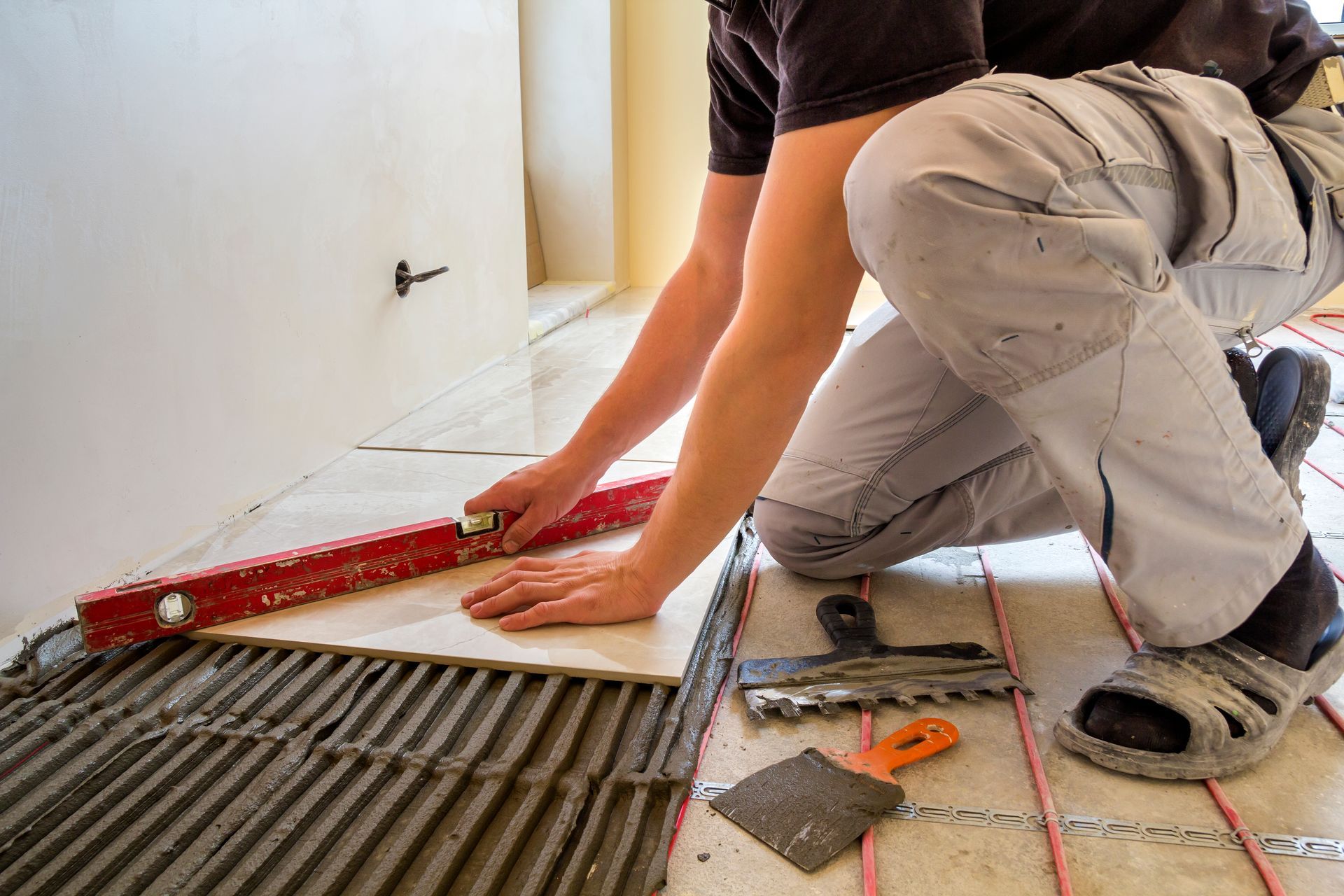 A man is kneeling down while laying tile on a floor.