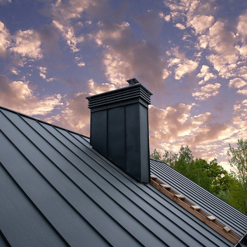Black metal roof with chimney against a cloudy sky.