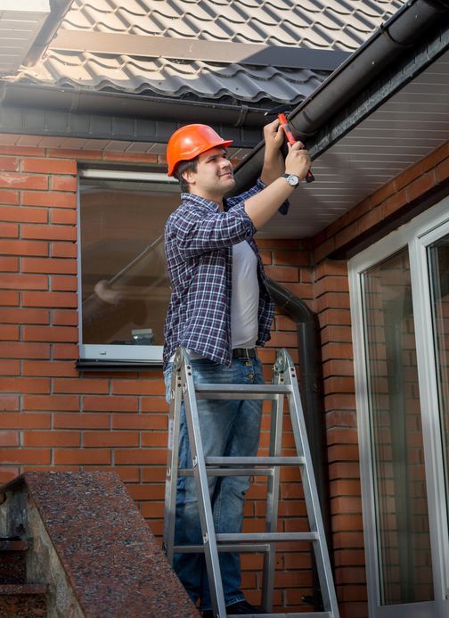 Young worker standing on step ladder and repairing gutter on house | Shiloh Roofing | PA