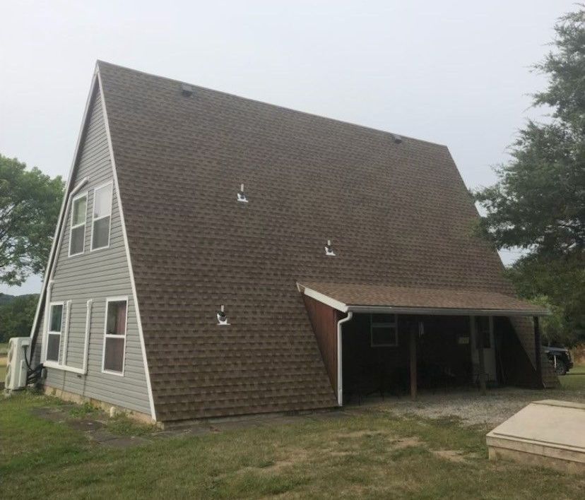 A large a frame house with a brown roof is sitting in the middle of a grassy field.