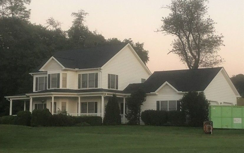 A large white house with a black roof is sitting on top of a lush green field.