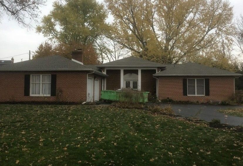 A brick house with a green dumpster in front of it.