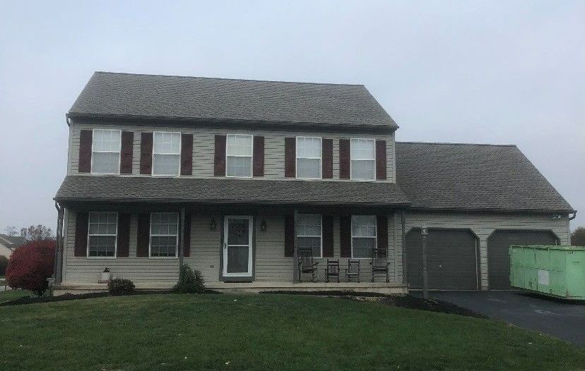 A large house with a gray roof and brown shutters is sitting on top of a lush green lawn.