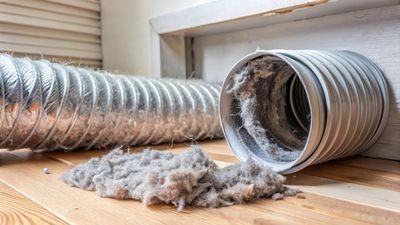 Dryer vent with lint buildup on a wooden floor, next to a flexible metal duct. Dryer vent with lint buildup on a wooden floor, next to a flexible metal duct.