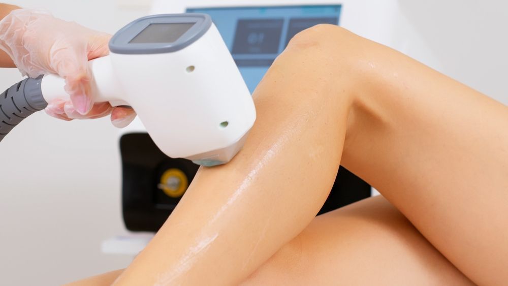 A person's leg is being treated with a laser hair removal device in a clinic setting.