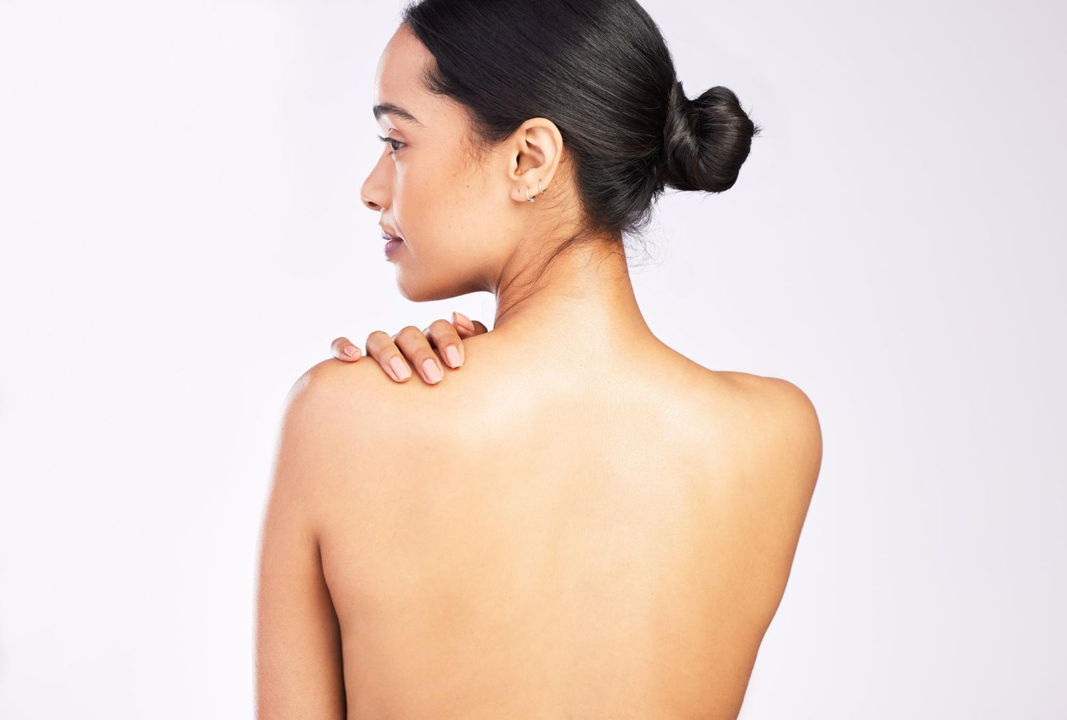 A woman without a shirt is standing with her hand on her shoulder.