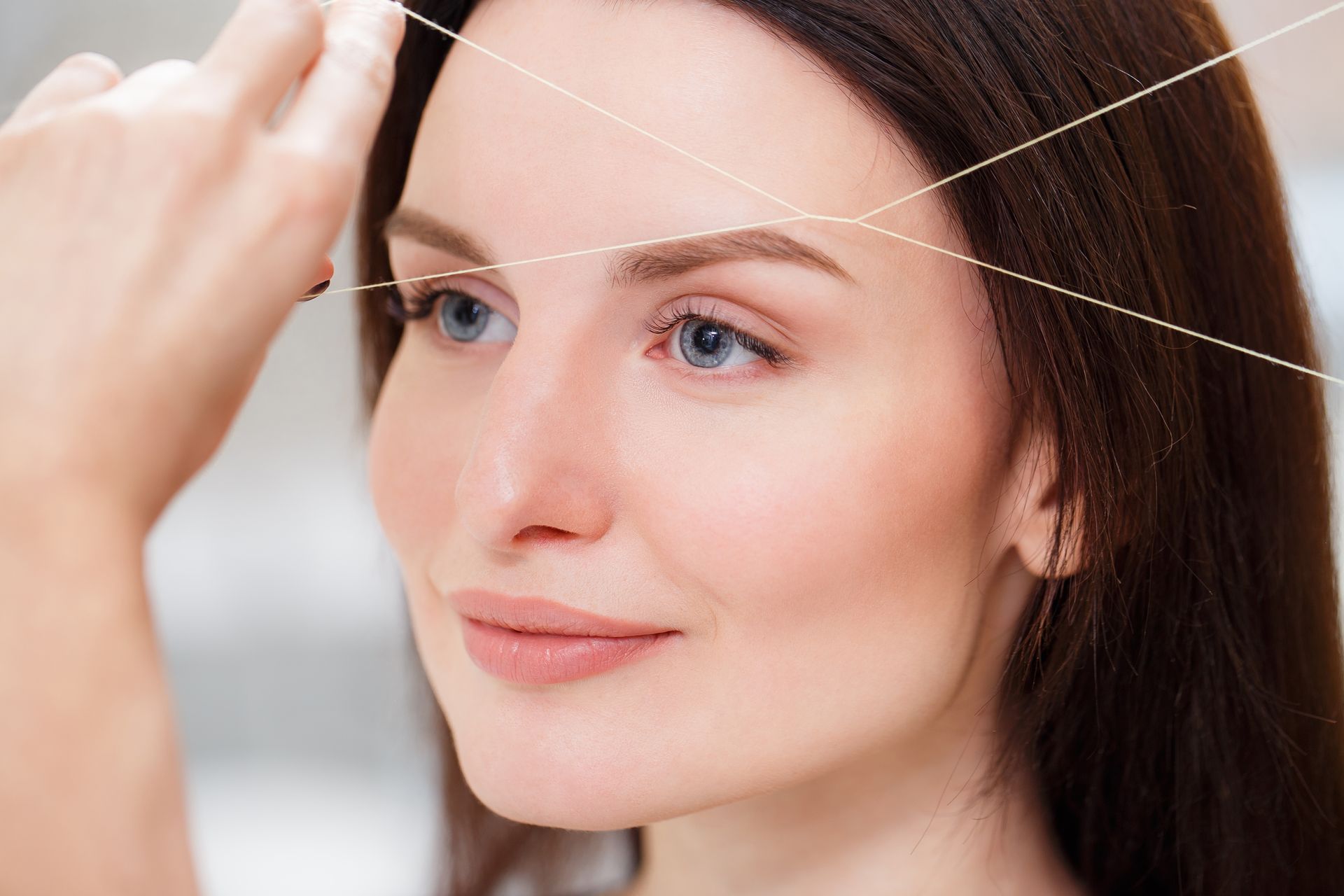 A woman is threading her eyebrows with a string.