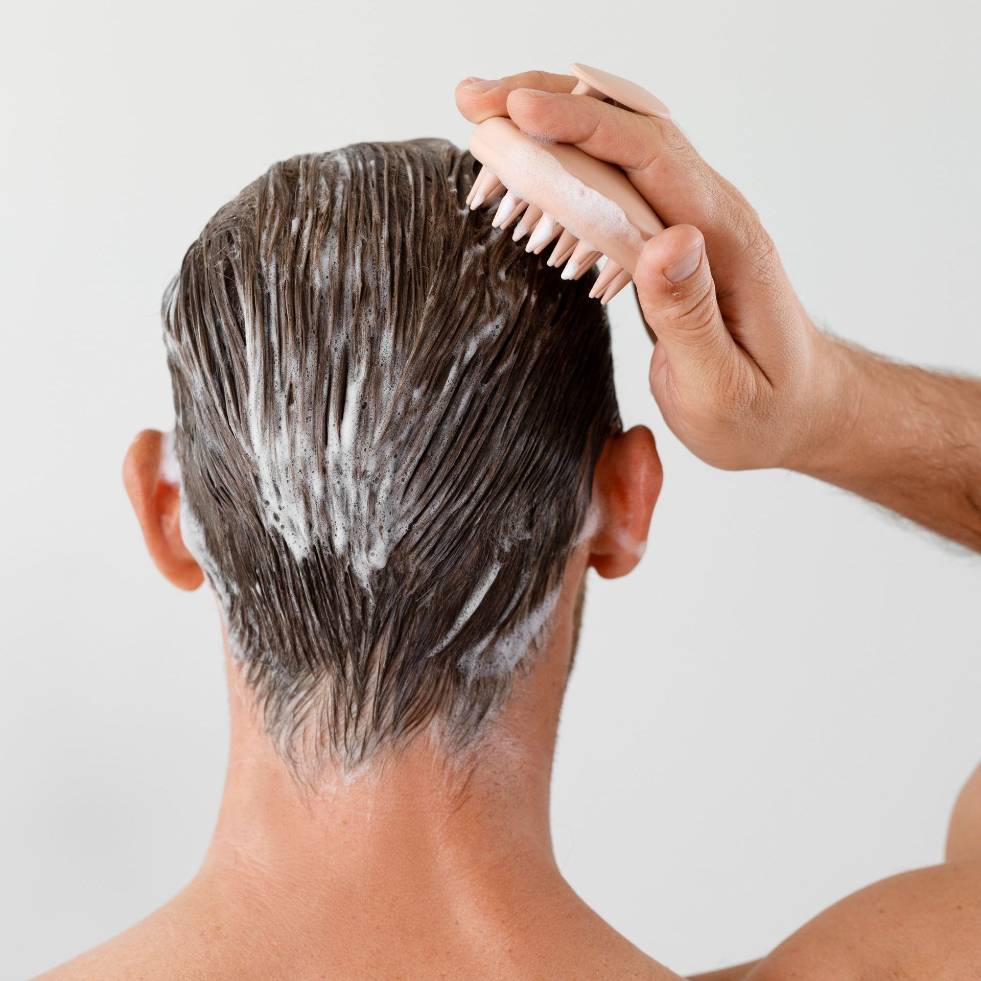 A man is washing his hair with a pink brush