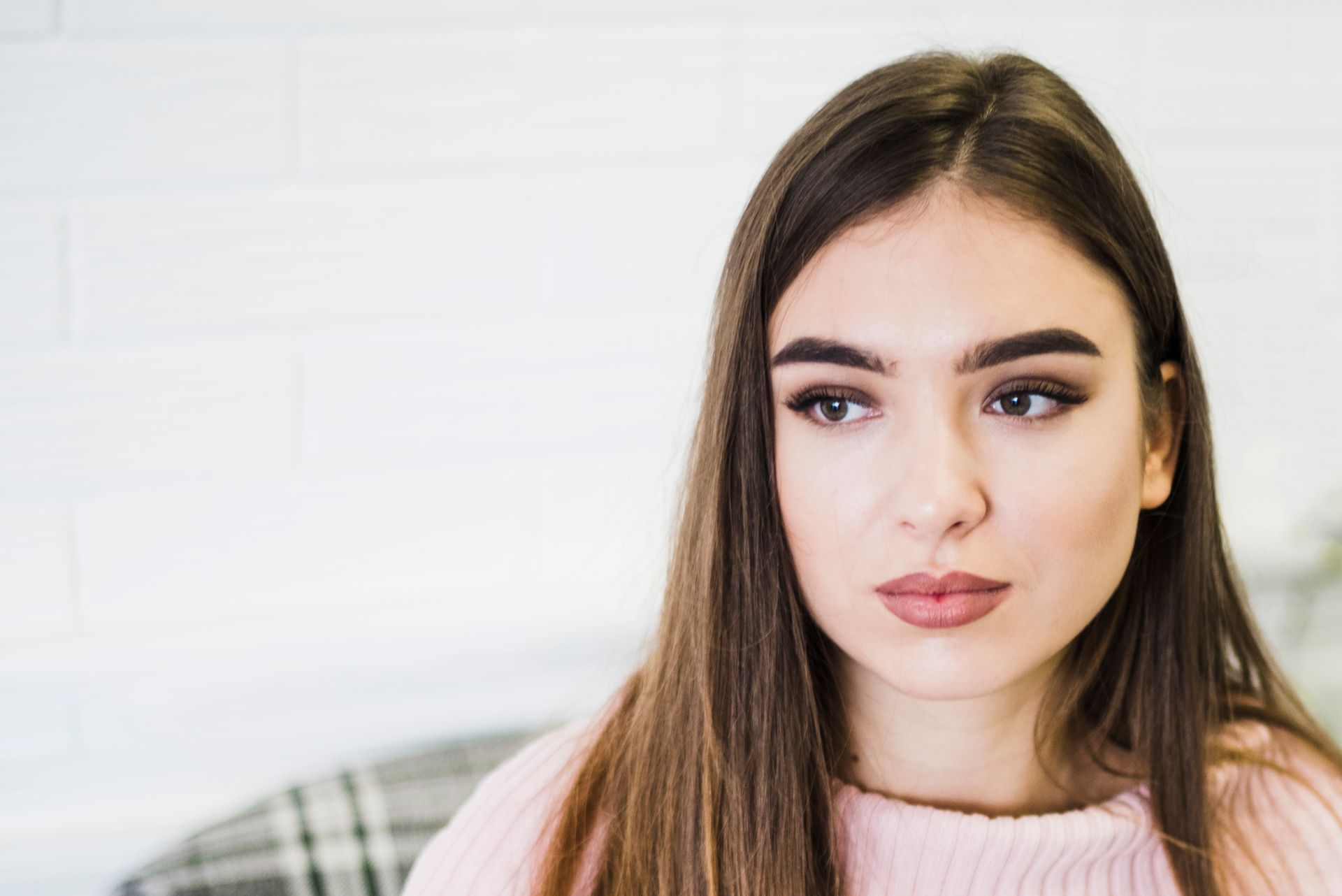 A woman in a pink sweater is sitting on a couch and looking at the camera.