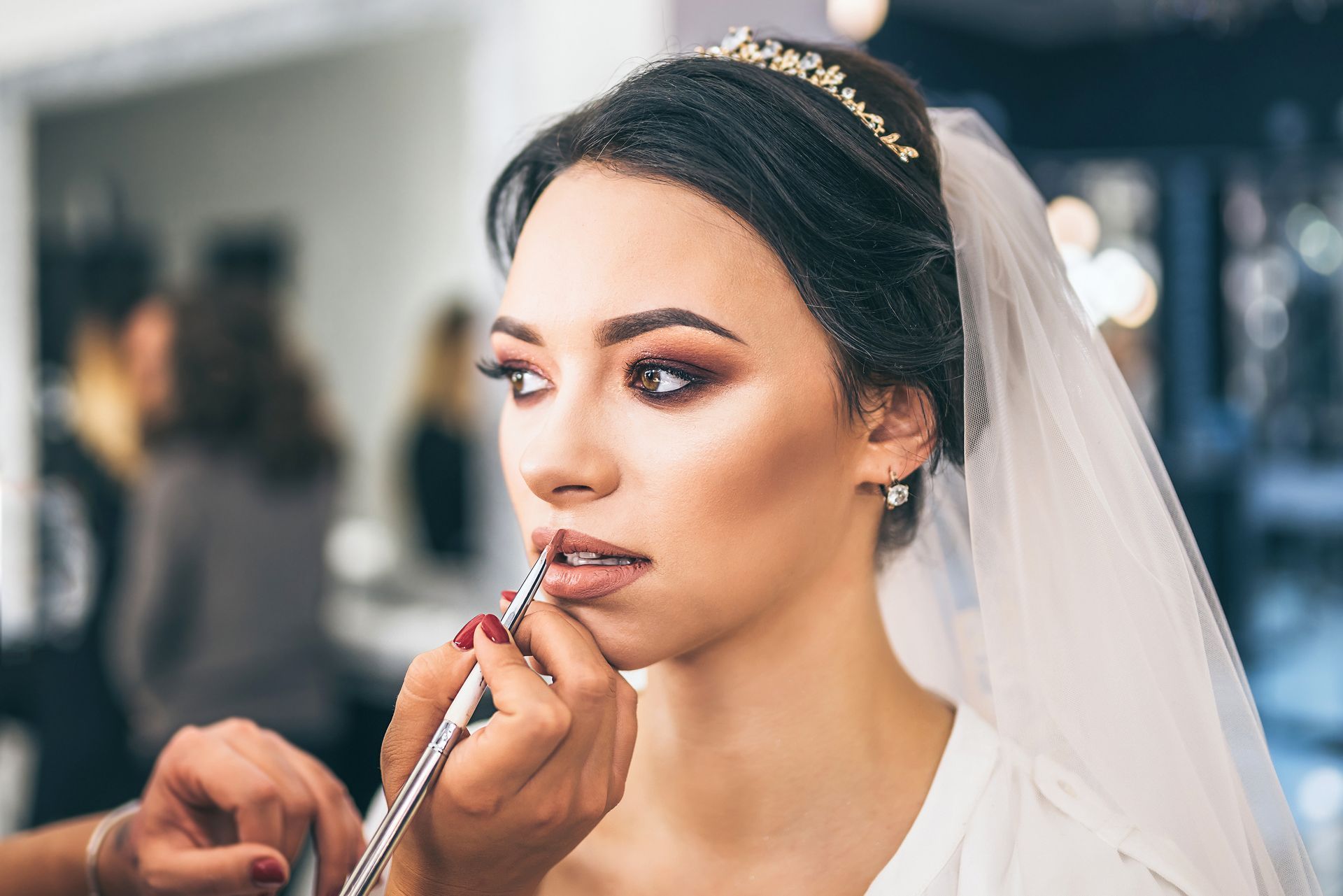 A bride is getting her makeup done by a makeup artist in a salon.