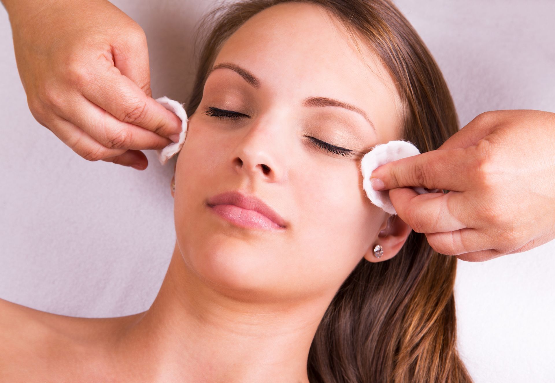 A woman is getting her face cleaned with cotton pads.