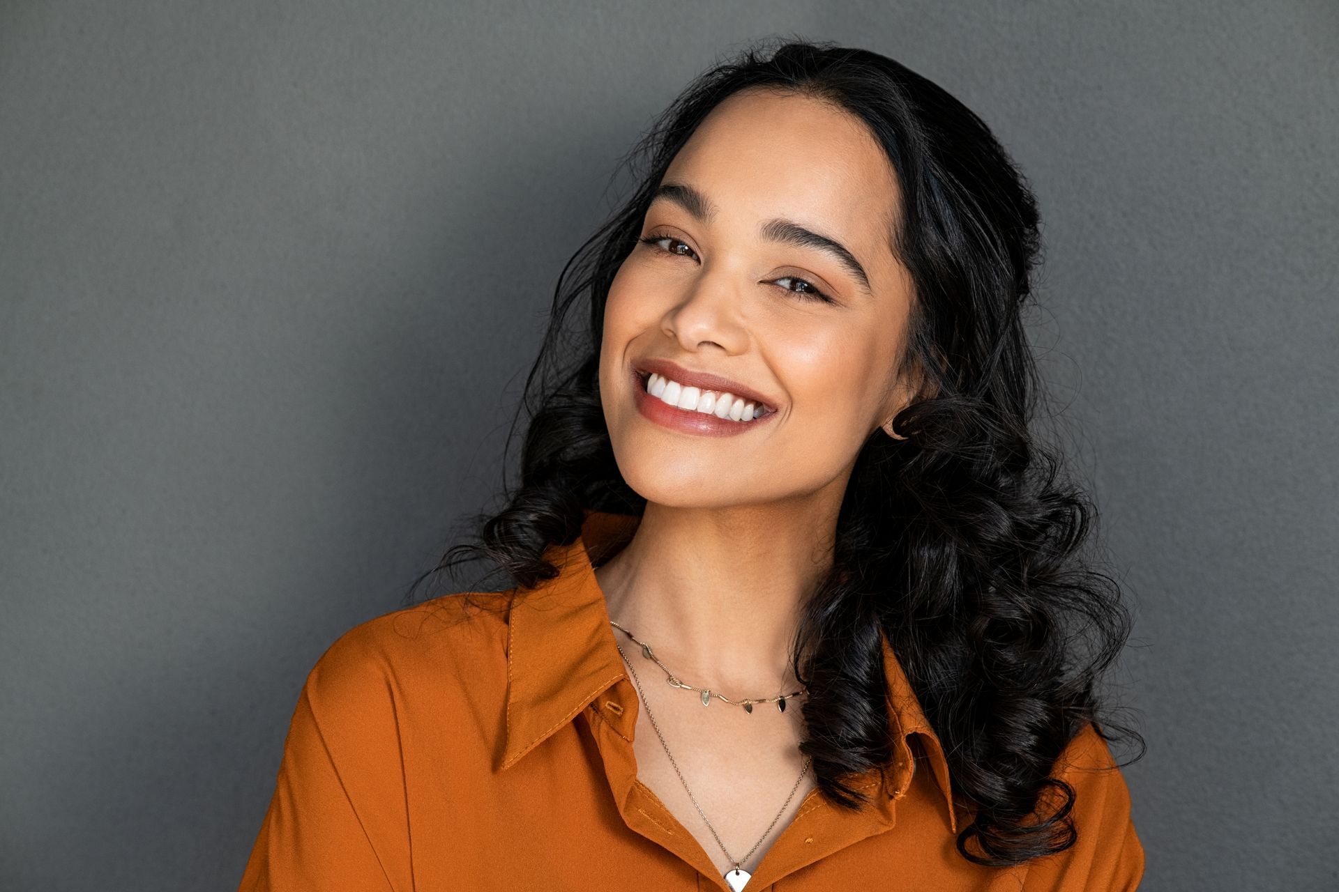 A woman in an orange shirt and necklace is smiling.