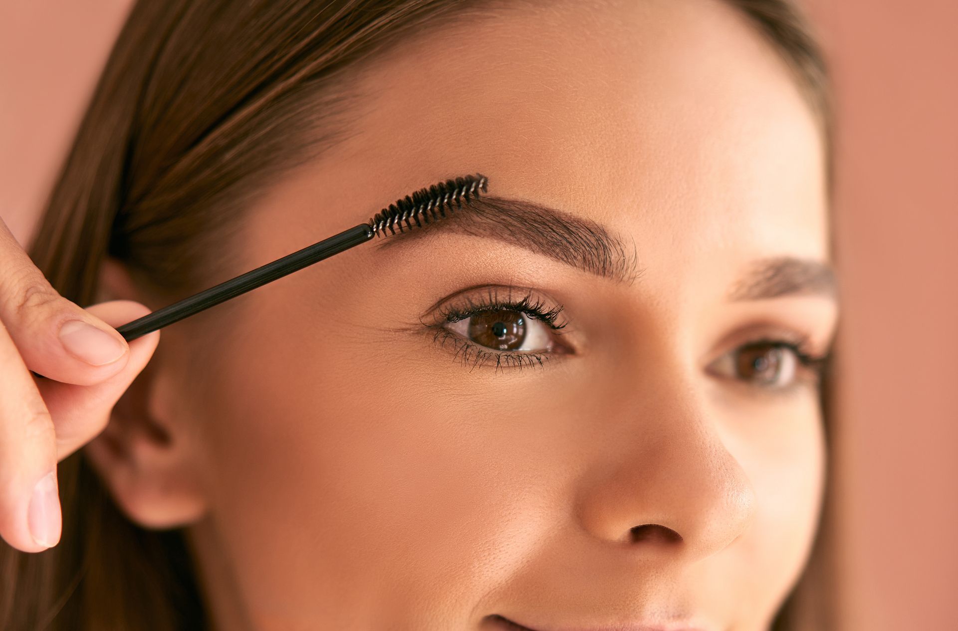 A woman is brushing her eyebrows with a brush.