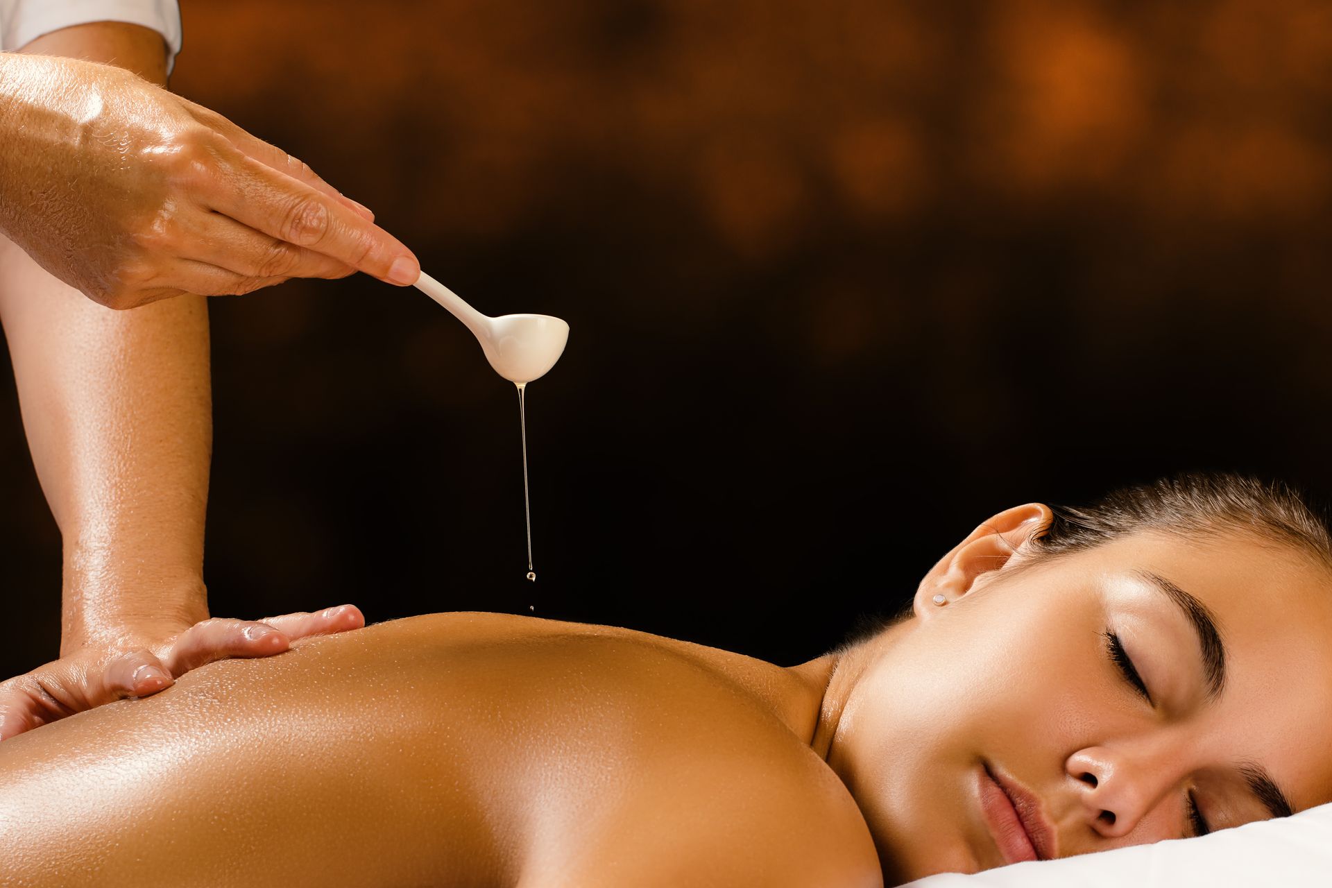 Massage therapist pouring oil onto a client’s back during a spa treatment