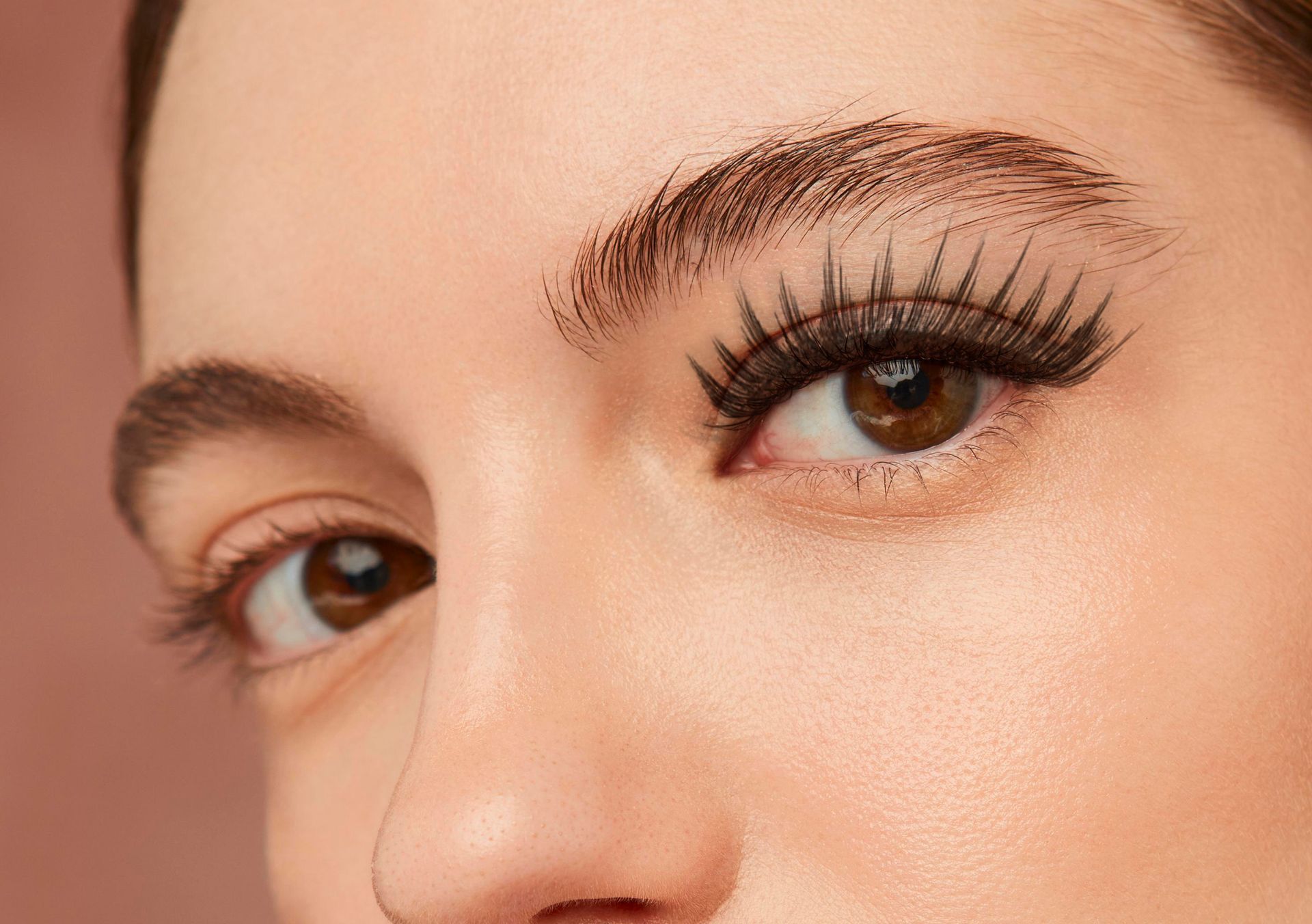 Close-up of a person's face; one eye with thick, dark eyelashes and eyebrow, other eye has natural lashes.