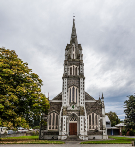 A large stone Gothic church with a steeple and a cross on top of it .