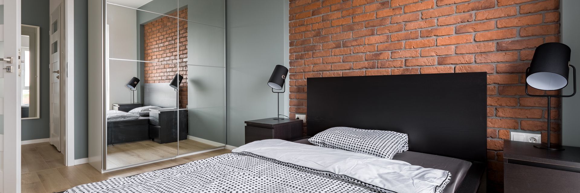 A bedroom with a brick wall , sliding glass doors , a bed , nightstands , and a lamp.