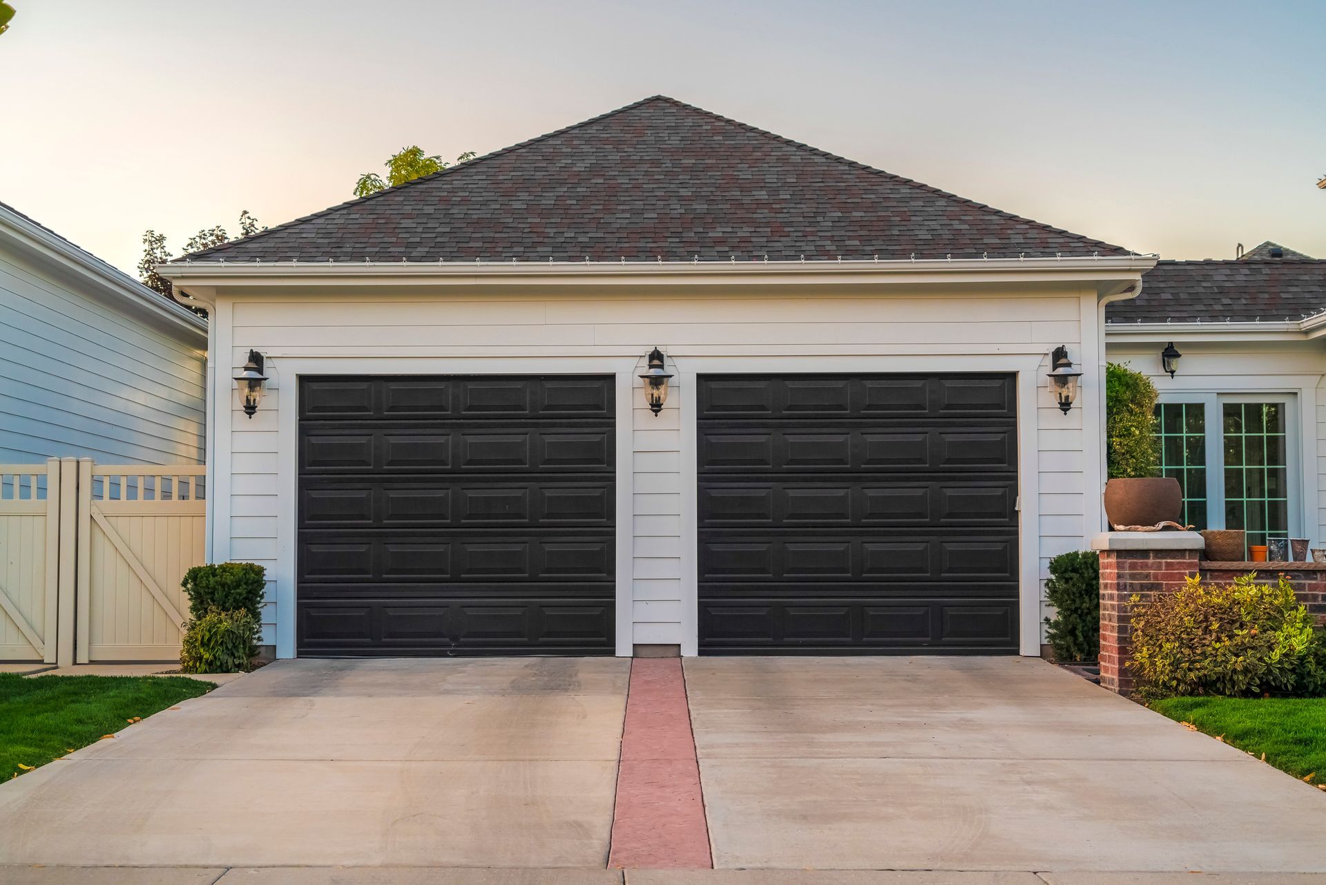 A white house with two black garage doors and a driveway.